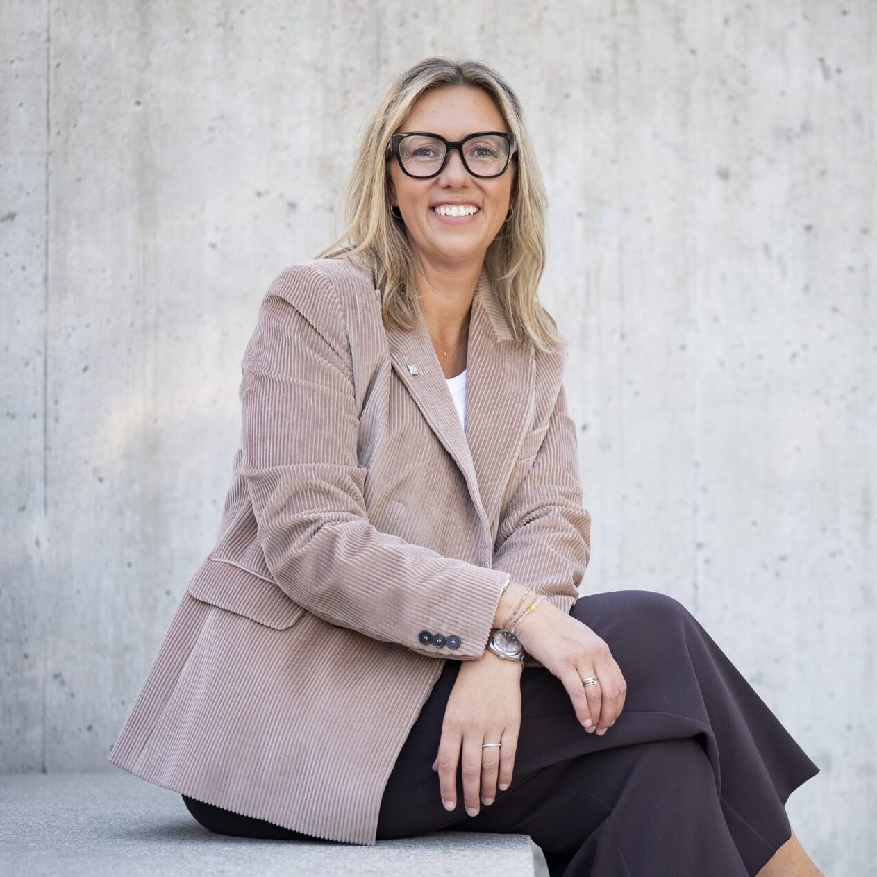 Frau mit Brille und Cordblazer sitzt auf einer Betonstiege